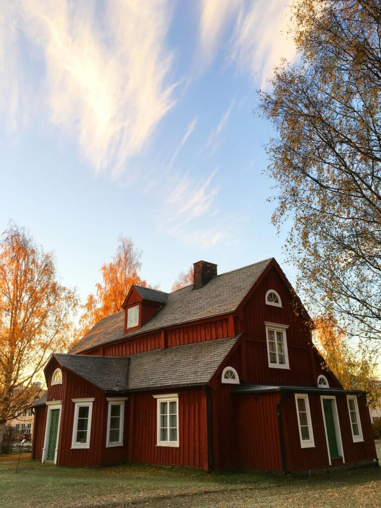 Picturesque red wooden house in autumn. Traditional Swedish architecture amidst colorful foliage.